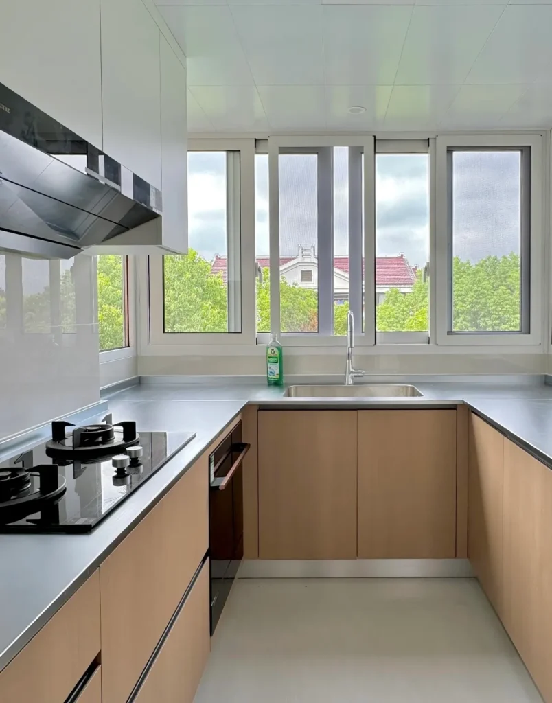 A bright, compact apartment kitchen featuring a U-shaped layout with light wood cabinets and a durable 2cm stainless steel countertop.