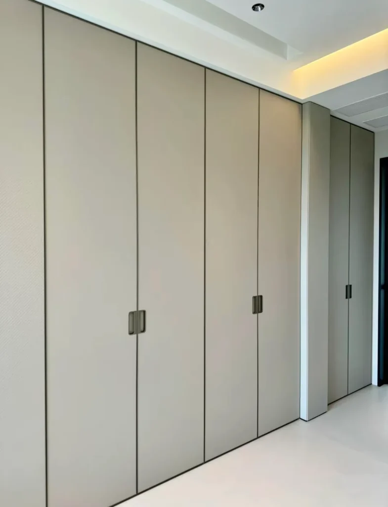 Full-wall custom fitted wardrobe featuring floor-to-ceiling matte grey panels and minimalist dark metal handles.
